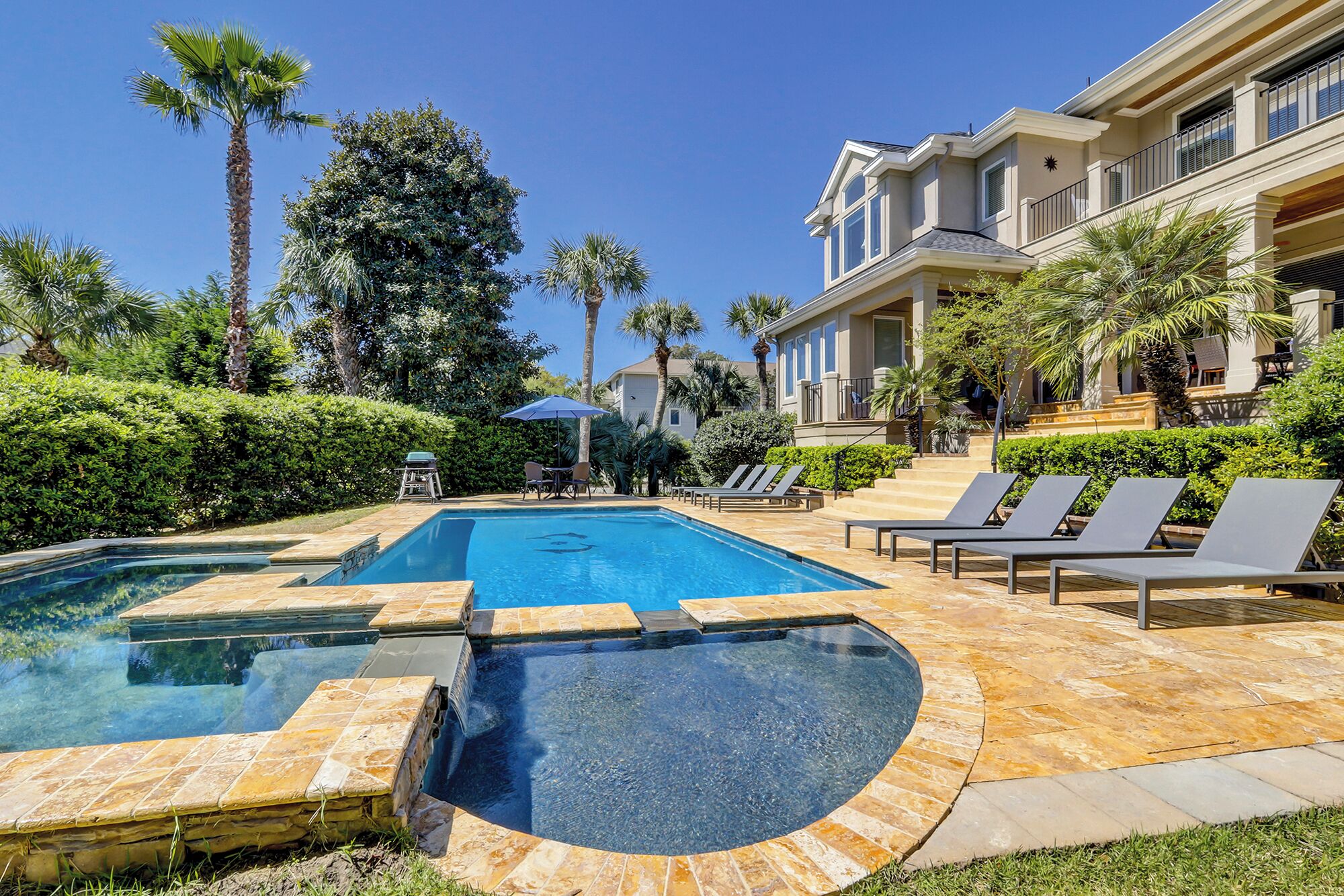 A swimming pool with a hot tub, surrounded by lounge chairs and palm trees.