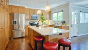 A modern kitchen with wooden cabinets, stainless steel appliances, and a central island with stools. - Perfect for Wine Country Vacation Living and Entertaining (Santa Rosa)