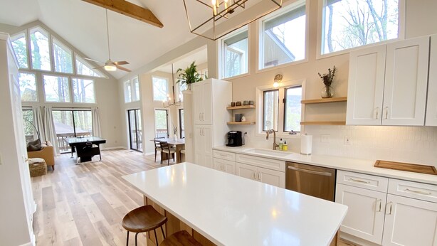 A spacious kitchen with a large island, wooden flooring, and white cabinetry. There are multiple windows providing natural light and views of the outdoors. - Enjoy Luxury & Games With A View (Maggie Valley)
