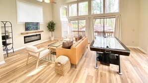 A spacious living room with a pool table, a sofa, a TV, and large windows. - Enjoy Luxury & Games With A View (Maggie Valley)