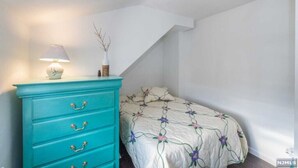 A bedroom with a bed, a turquoise dresser with drawers, a lamp, and a vase with branches. - Cozy & Quiet 2 Bed Apt 20 Minutes to NYC (Fort Lee)