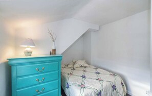 Ein Schlafzimmer mit einem Bett, einer türkisfarbenen Kommode mit Schubladen, einer Lampe und einer Vase mit Zweigen.
