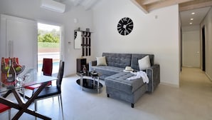 A modern living room with a grey sofa, a glass dining table, and a black clock on the wall. - Villa Ventus Sleeps 7 With Parking (Corfu)