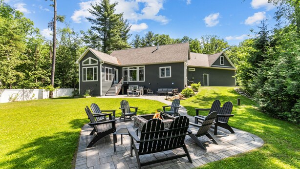 Ein Haus mit einer Terrasse, Adirondack-Stühlen und einem Feuerkorb.