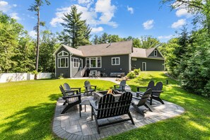 Une maison dotée d’un patio aménagé avec des fauteuils Adirondack et un foyer extérieur.