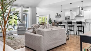 Eine moderne Küche mit weißen Schränken, schwarzen Barhocker und einem grauen Sofa in einem großzügigen Wohnbereich.
