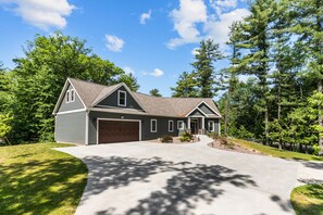 A two-story house with a garage, a driveway, and a well-maintained lawn. - Family Friendly lake home, beach, level lot, fire pit, game room, dog friendly! (Coloma)