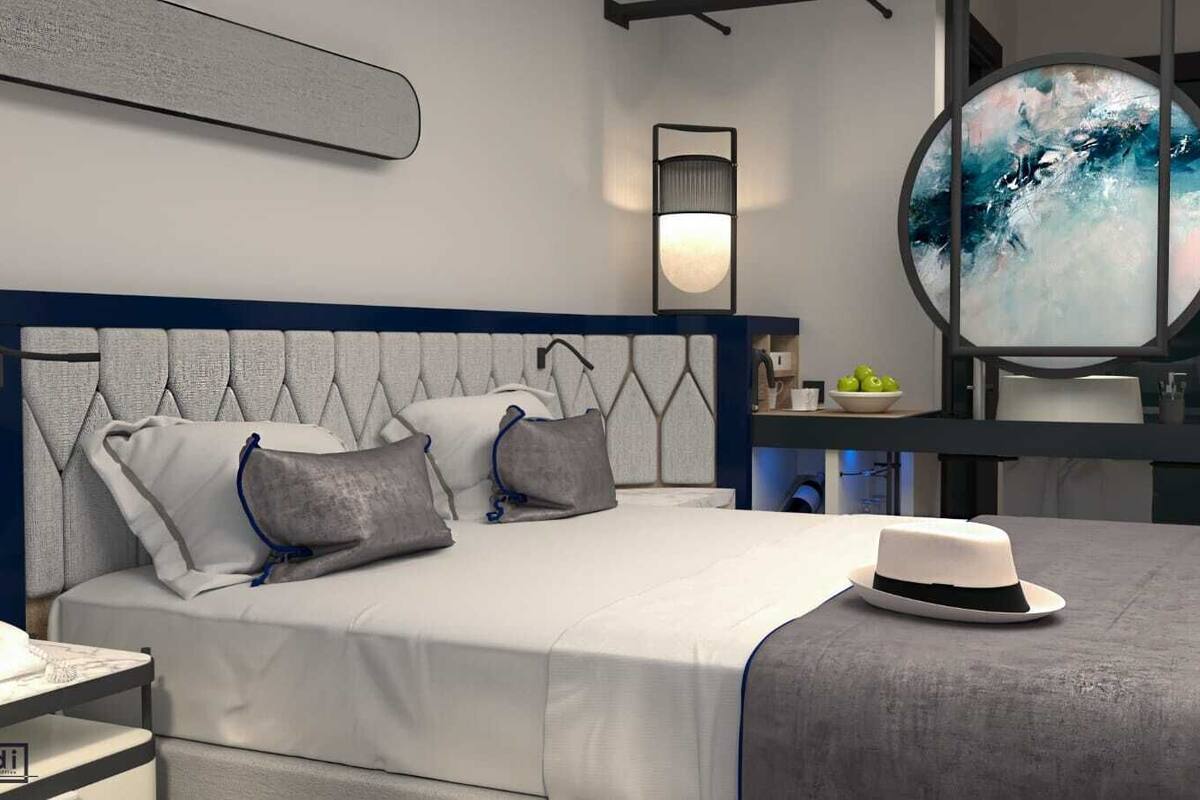 A modern bedroom with a tufted headboard, a bedside table with a telephone, and a round mirror with a painting above it.