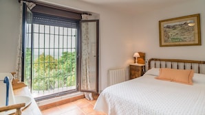 A bedroom with a bed, a nightstand, a window with a view, and a painting on the wall. - Cortijo Don Simon, ideal for families and friends (pet friendly) (Cabra)