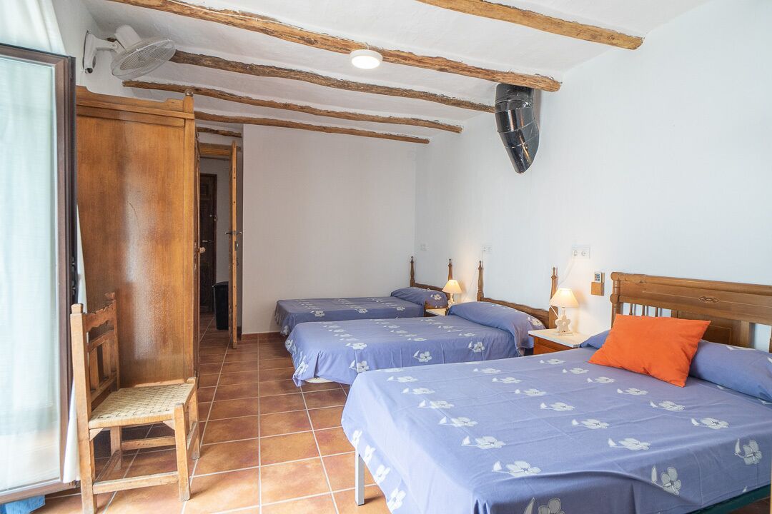 A room with two beds, a wooden chair, a ceiling fan, and a door leading to another room.