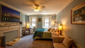 A hotel room with a bed, a desk, a chair, a fireplace, and a cityscape painting on the wall. - Gorgeous Beacon Hills Studio next to State house (Boston)