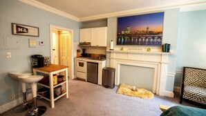 A compact kitchen with white cabinets, a dining area with a small table and bar stools, a fireplace, and a cityscape painting on the wall. - Gorgeous Beacon Hills Studio next to State house (Boston)