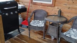 A wooden cabin with a grill, wicker chairs, and a window.