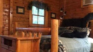 A log cabin room with a bed, a wooden chest of drawers, and a window with a view.