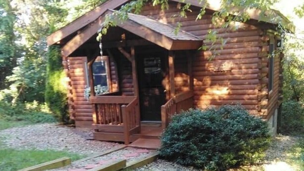 A rustic log cabin with a porch, a small front door, and a wooden walkway leading to the entrance.