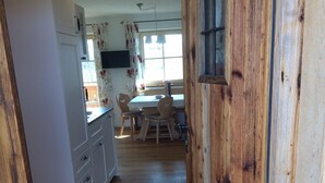 En træbeklædt indgangshal, der fører til et spiseområde med et bord og stole. Et velkomstskilt er synligt i enden af hallen.