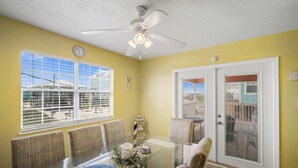 A dining area with a glass table, chairs, a ceiling fan, and windows with blinds. - Coral Breeze (Fort Morgan)