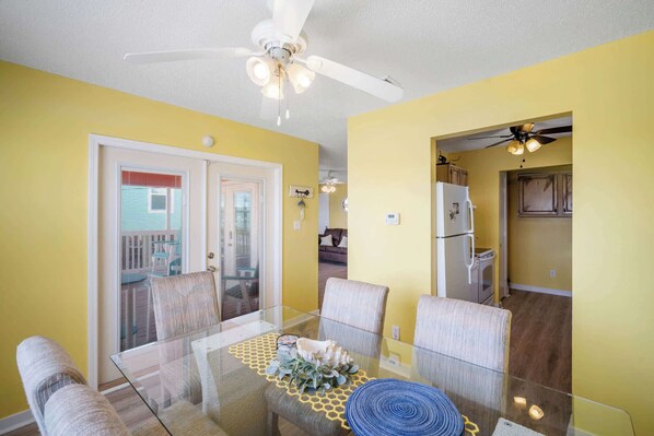 A dining area with a glass table, chairs, and a ceiling fan.