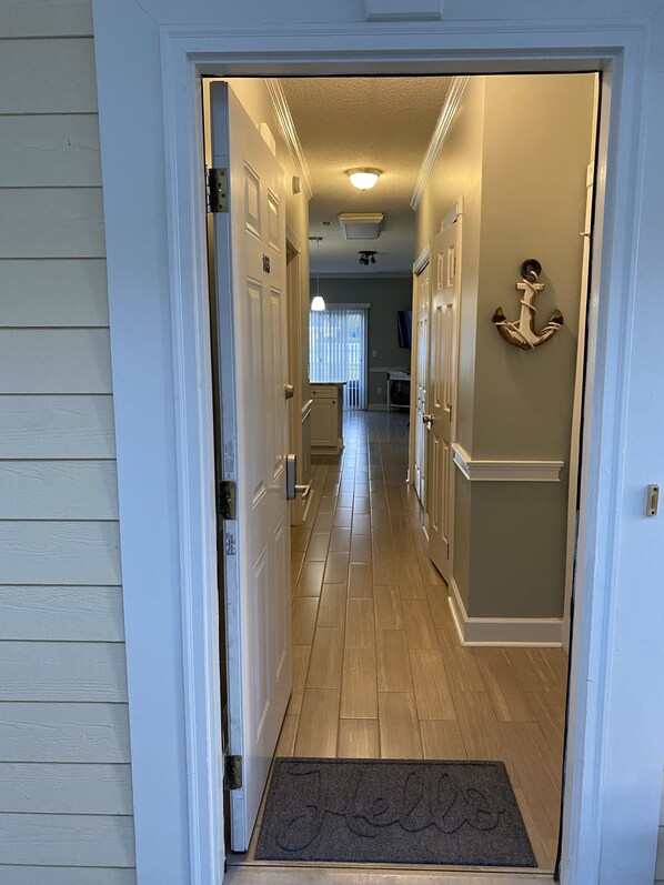 A hallway with a wooden floor, white doors, and a doormat with the word "Welcome".