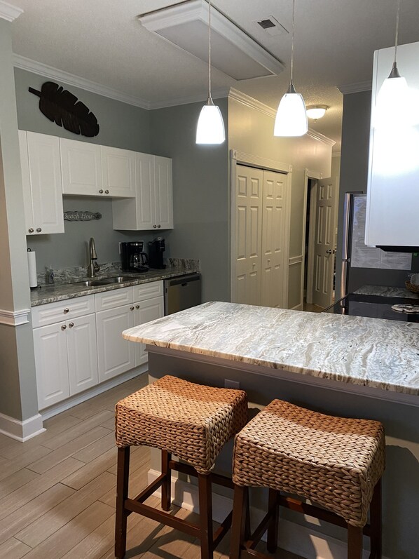 A kitchen with white cabinets, a marble countertop, two woven stools, and pendant lighting.