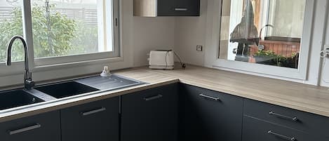 A modern kitchen with dark cabinets, a sink, and a window overlooking a garden.