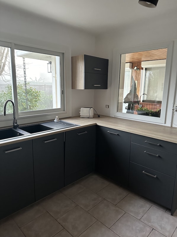 A modern kitchen with dark cabinets, a sink, and a window overlooking a garden.