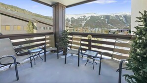 A balcony with a view of snow-capped mountains, a small table, and two chairs.
