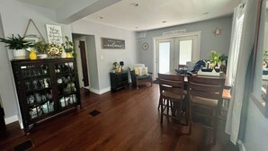 A spacious living area with a wooden floor, a dining table with chairs, and a kitchen area visible through an open door. - Convenient to every event that Louisville hosts! (Audubon Park)