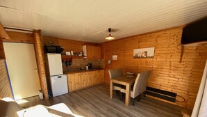 A compact kitchen with wooden cabinets, a dining table, and a refrigerator.