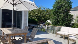 Une terrasse en bois avec une table et des chaises, un parasol blanc et un canapé blanc.