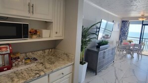 A modern kitchen with white cabinets, a granite countertop, and a dining area with a view. - Serenity by the Sea. Oceanfront. (Myrtle Beach)