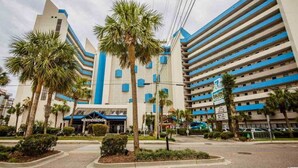 A hotel with multiple floors, palm trees, and a blue and white color scheme. - Serenity by the Sea. Oceanfront. (Myrtle Beach)