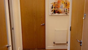 A hallway with wooden flooring, white walls, and a radiator. - By the seaside (London)
