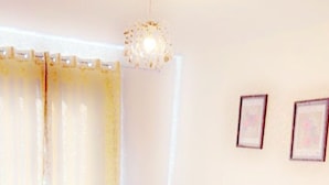 A bedroom with a large bed, a bedside table, a nightstand, a hanging light fixture, and two framed pictures on the wall. - By the seaside (London)