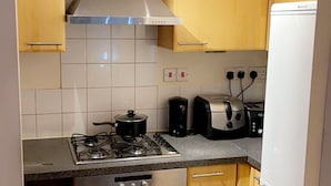 A compact kitchen with a gas stove, oven, toaster, and a white refrigerator. - By the seaside (London)