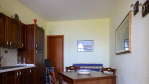 Un coin repas avec une table en bois, des chaises et un saladier bleu et blanc. On y trouve également un buffet en bois sur lequel est posé un objet décoratif rouge. Un tableau encadré est accroché au mur, et un miroir est fixé au-dessus de la table.