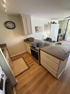 Une cuisine moderne avec un plancher en bois, des meubles blancs, un four encastré et un grand îlot central doté d’un comptoir.