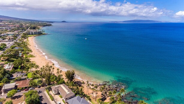 Una vista aerea di una zona costiera con una spiaggia, edifici residenziali e una limpida visuale sull'oceano.