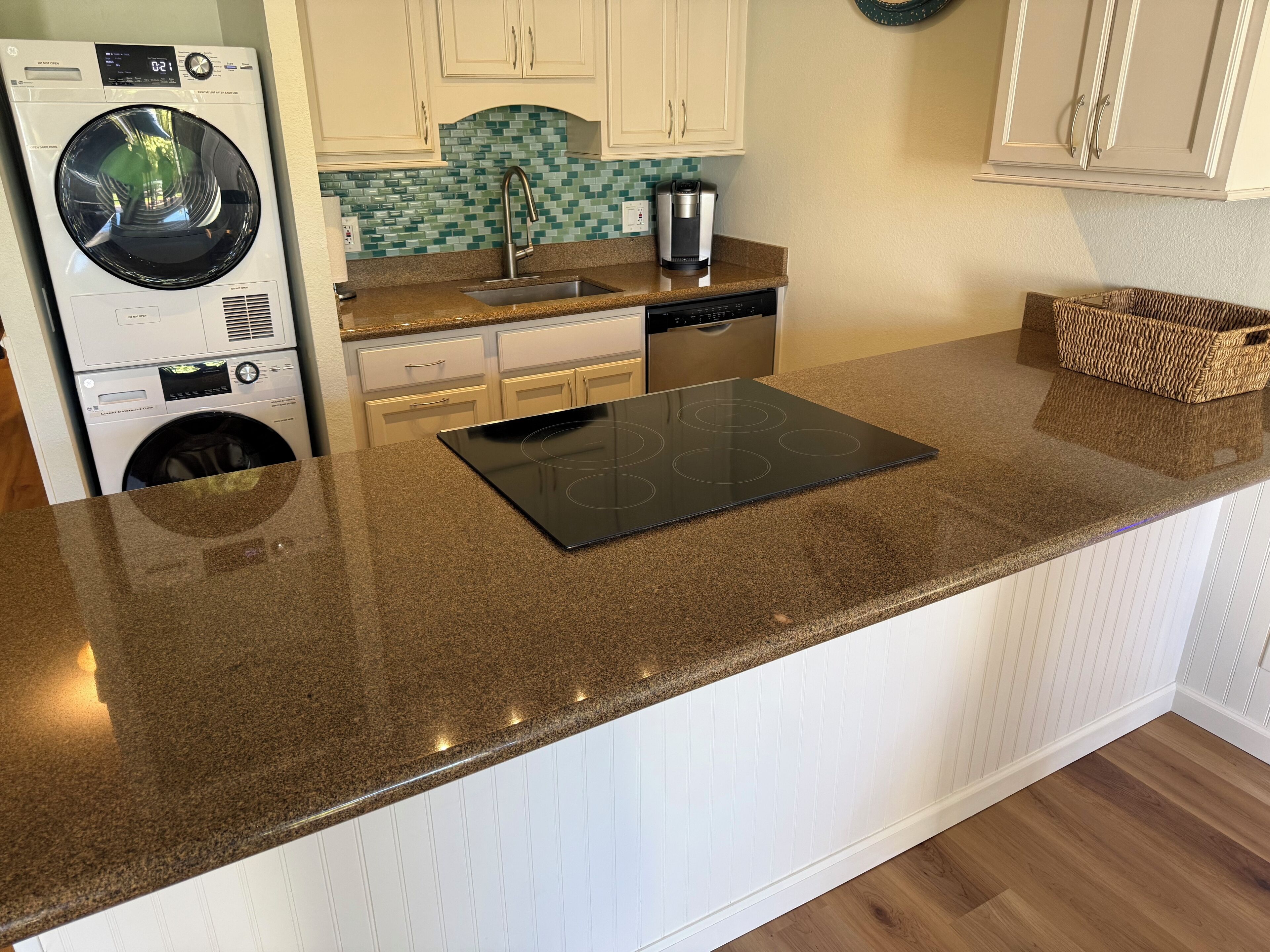 A kitchen with a granite countertop, a built-in oven, a washing machine, and a coffee maker.