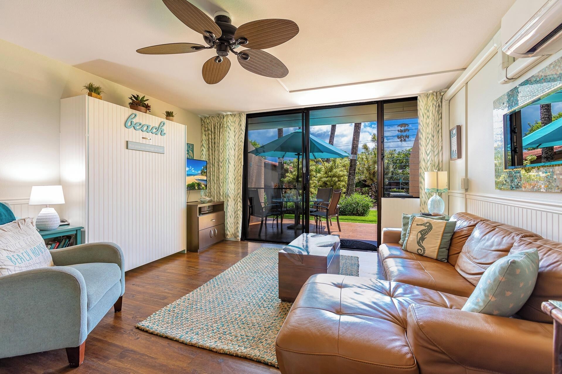 A living room with a sofa, a chair, a glass door leading to a patio, a ceiling fan, and a sign on the wall.