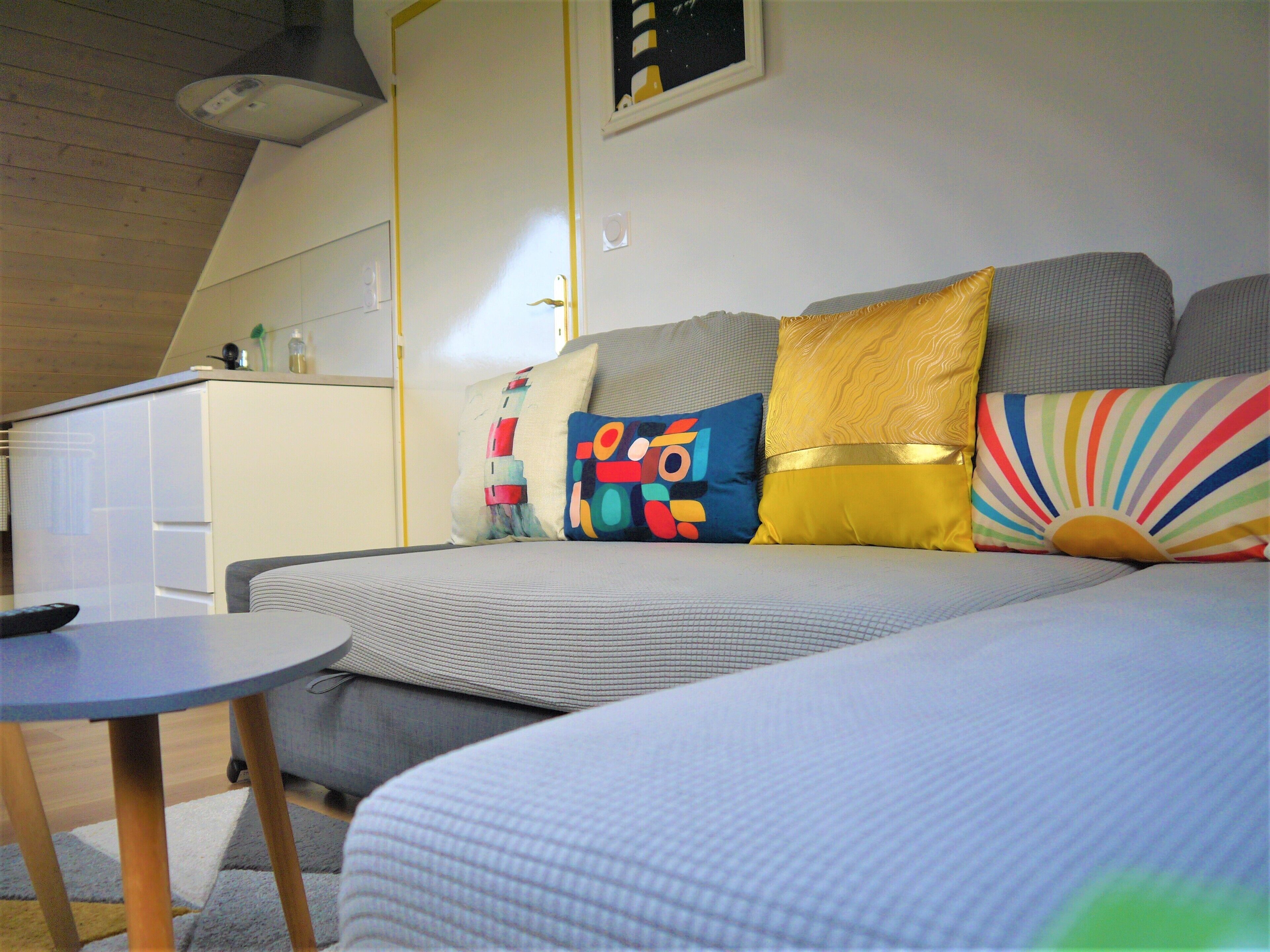 Een gezellige kamer met een bank, een kleine tafel en een kitchenette op de achtergrond.