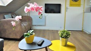 Ein modernes Wohnzimmer mit einer Couch, einem an der Wand befestigten Fernseher und zwei Blumentöpfen auf Beistelltischen.