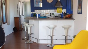 A modern kitchen with a bar area, wooden flooring, and a bright yellow armchair. - Loft 80m2 top floor 100m beach & center Bandol (Bandol)