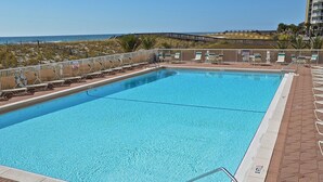 Et rektangulært swimmingpool med krystalklart blåt vand, omgivet af en flisbelagt terrasse og liggestole.