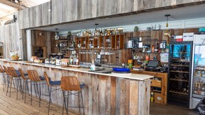 A rustic bar area with wooden walls, a long counter, and wicker bar stools. - Villa Ocean - Indulge Yourself in Paradise (Indigo Bay)
