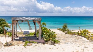 A beach with a wooden gazebo, a lounge chair, and a small table. - Villa Ocean - Indulge Yourself in Paradise (Indigo Bay)