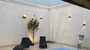 Een zwembadgedeelte met twee ligstoelen, een kleine plant en wandlampen.