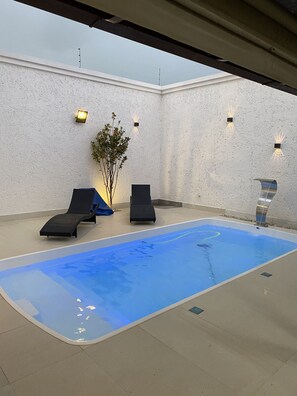 Ein Poolbereich mit zwei Liegestühlen, einer kleinen Pflanze und Wandleuchten.