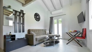 A modern living room with a sofa, a coffee table, a TV, and a dining area with a red chair. - Villa Bratou Terra (Corfu)