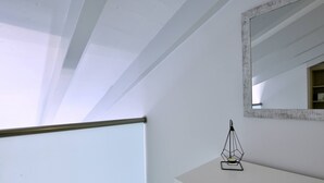 A room with a white ceiling, a white wall, a wooden door, and a white counter with a geometric candle holder. - Villa Bratou Terra (Corfu)